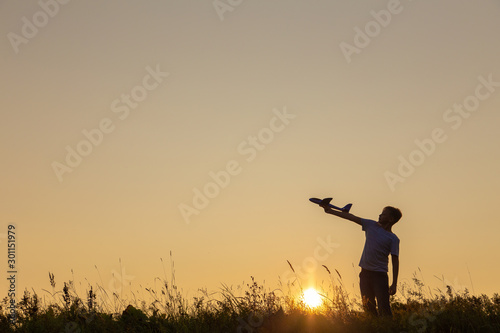 Black silhouette of cute little kid holding big toy plane in hand isolated at sunny orange sunset sky background. Horizontal color image. 