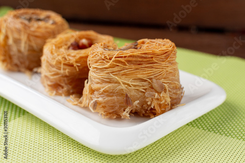Traditional Oriental sweet bird's nest with honey and nuts close-up. Sweet roll of thin dough. Selective focus. On a wooden background and a green napkin.