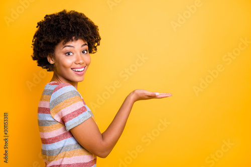 Profile photo of amazing dark skin lady holding new offer price product on open palm wear casual striped t-shirt isolated on yellow background photo