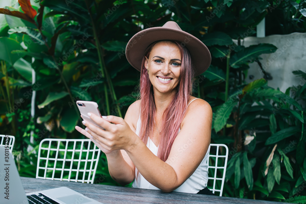 Fototapeta premium Smiling woman browsing cellphone on greenery background
