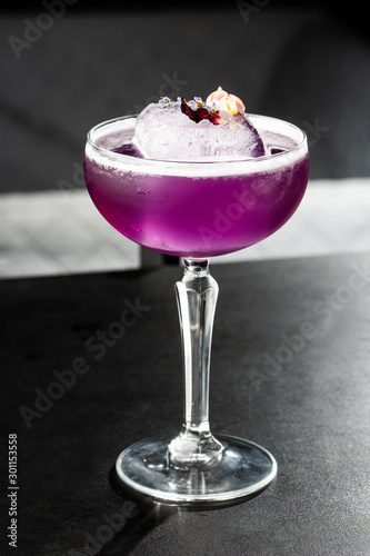 Homemade Purple Cocktail with a Large Ice Cube on black background. Close up of purple cocktails in a glass of margaritas with sugar edges, violet and protein foam. Vertical photo.