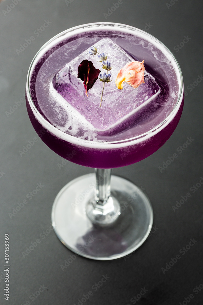 Homemade Purple Cocktail with a Large Ice Cube on black background. Close up of purple cocktails in a glass of margaritas with sugar edges, violet and protein foam. Vertical photo.