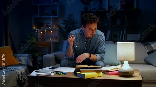 Young man spinning a pencil while studying at home at night