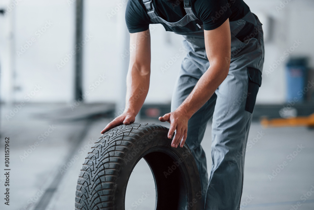 Fototapeta premium Photo in motion. Mechanic holds a tire at the repair garage. Replacement of winter and summer tires