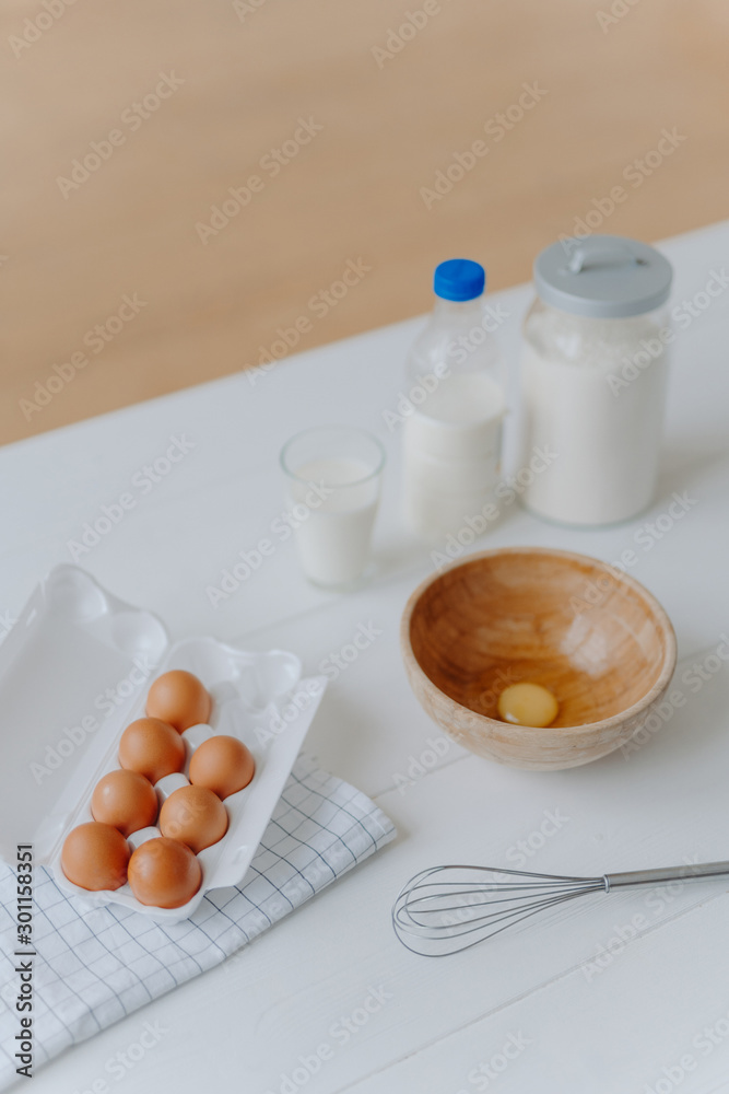 Top view of different dough recipe ingredients at kitchen table. Eggs, whisk, glass of milk and flour. Cooking, baking and culinary concept. Top view of different dough recipe ingredients at kitchen table. Eggs, whisk, glass of milk and flour. Cooking, baking and culinary concept.