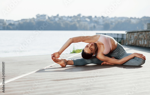 Human body flexibility. Young woman does exercises against lake