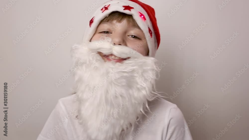 eight-year-old caucasian girl with artificial beard in Santa Claus hat with blinking red lights is smiling and laughing on white background. Funny child costume for celebrating new year and christmas eight-year-old caucasian girl with artificial beard in Santa Claus hat with blinking red lights is smiling and laughing on white background. Funny child costume for celebrating new year and christmas