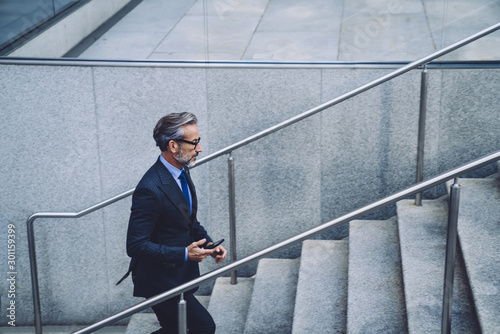 Middle-aged businessman on stairs with smartphone in city