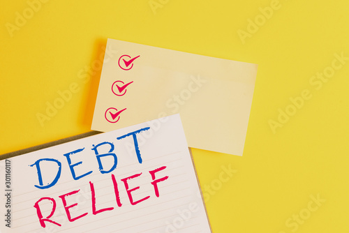 Conceptual hand writing showing Debt Relief. Concept meaning a reduction in the amount of debt that a country has to pay Empty orange paper with copy space on the yellow table