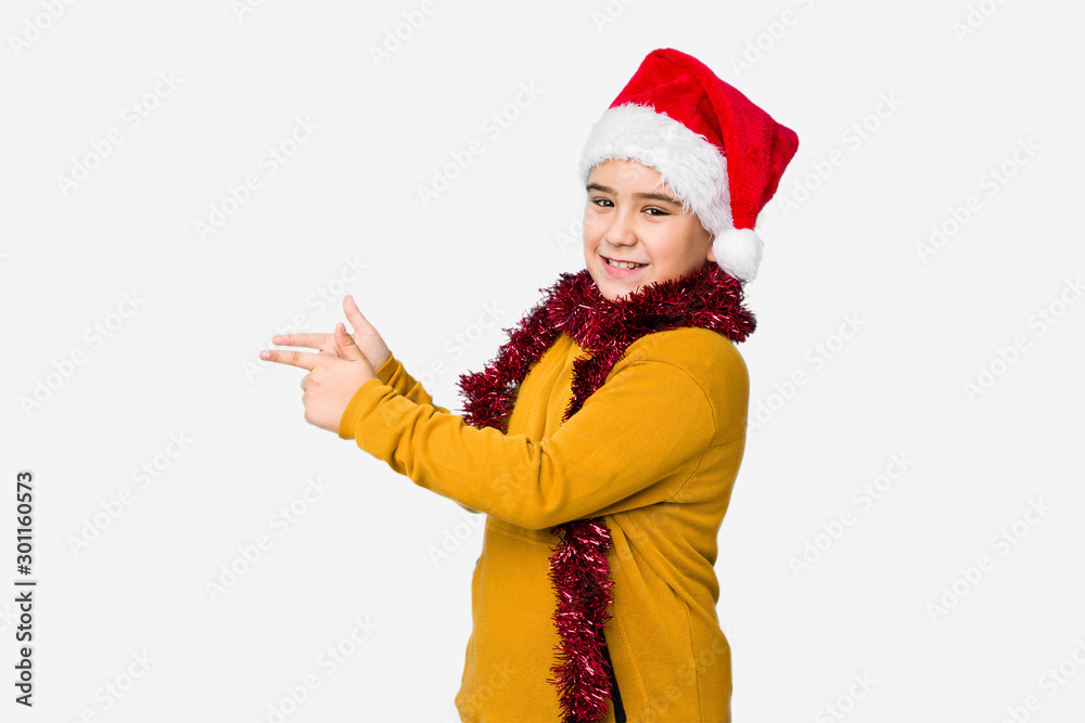Little boy celebrating christmas day wearing a santa hat isolated excited pointing with forefingers away. Little boy celebrating christmas day wearing a santa hat isolated excited pointing with forefingers away.