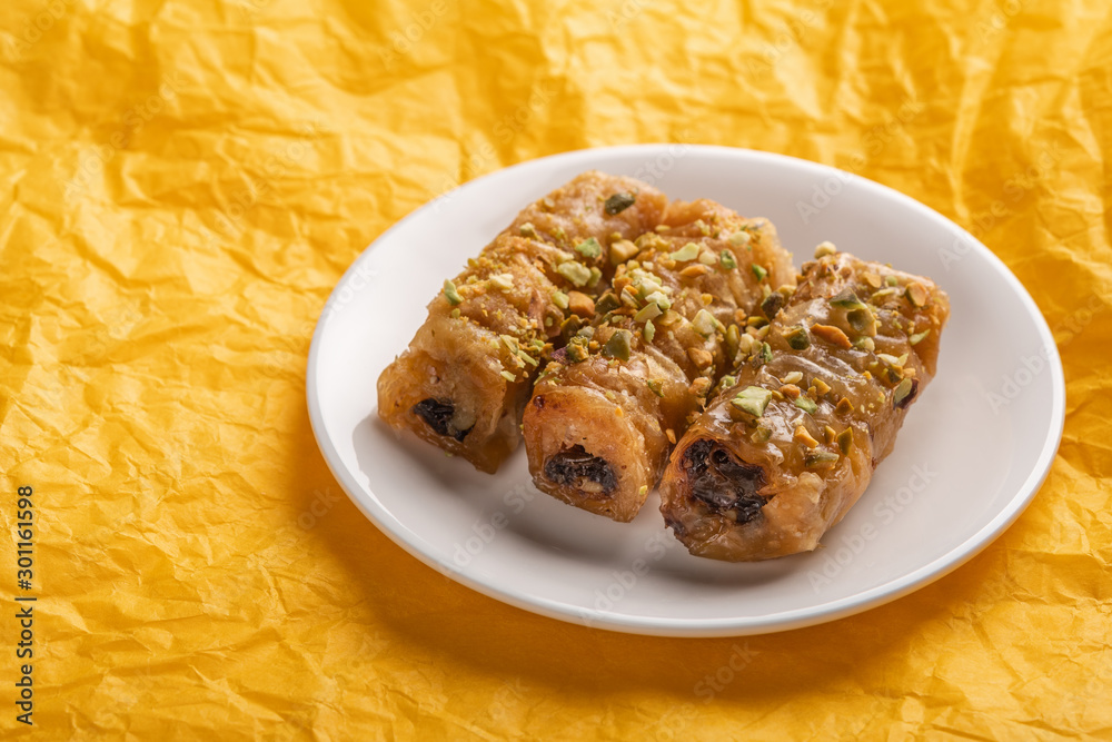Traditional greek pastry saragli in a white plate on a yellow paper background Traditional greek pastry saragli in a white plate on a yellow paper background