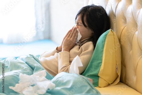 Sick child girl have a cold,blowing nose in paper handkerchief in bedroom,flu or the weather is changing,asian female teenage sneezing in a tissue,concept of allergic rhinitis,hay fever,health care