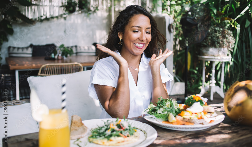 Young ethnic woman smiling with raised hands while sitting at table Young ethnic woman smiling with raised hands while sitting at table