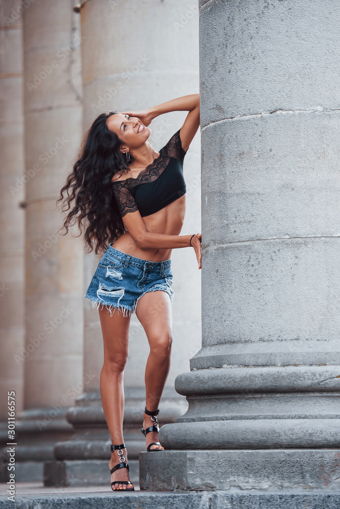 In shorts. Beautiful woman with curly black hair have good time in the city at daytime In shorts. Beautiful woman with curly black hair have good time in the city at daytime