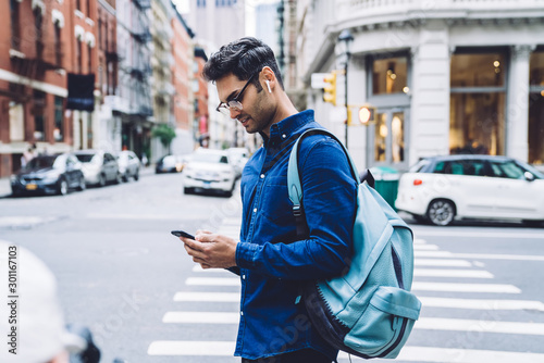 Canvas Print Ethnic young man using smartphone on street while walking