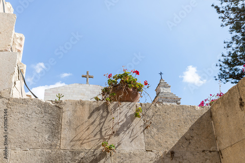 A pot of geraniums stands on wall against the background of the crosses of Monastery Carmel Pater Noster located on Mount Eleon - Mount of Olives in East Jerusalem in Israel photo