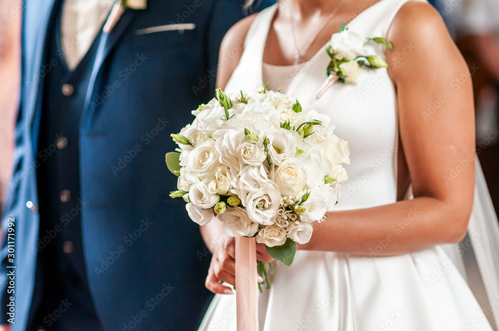 Groom and bride holding hands on the bouquet of flowers
