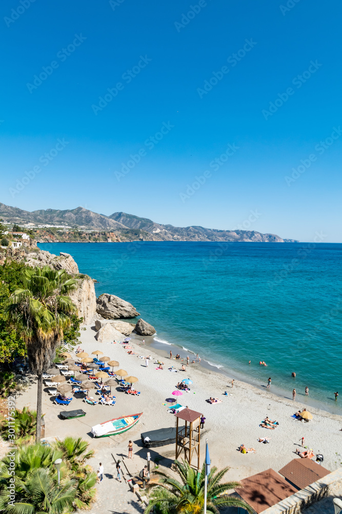 a summer beach scene taken from El Balcon de Europa overlooking one of the small beaches of Nerja, Spain 