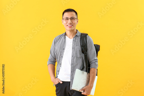 Male Asian student with laptop on color background