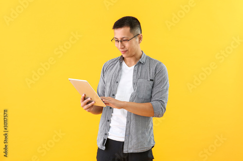 Male Asian programmer with tablet computer on color background