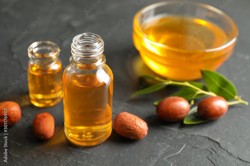 Jojoba oil and seeds on dark grey table Jojoba oil and seeds on dark grey table