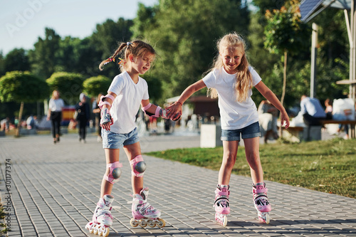Two cute kids riding by roller skates in the park at daytime