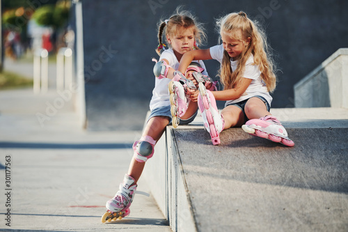 Warm weather. On the ramp for extreme sports. Two little girls with roller skates outdoors have fun