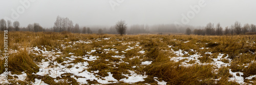 Panorama of the first snow lying in a meadow surrounded by forest. Smolensk region, Russia.