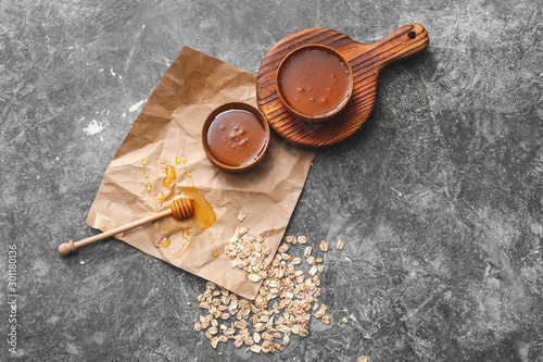 Bowls with tasty honey and oats on grey background