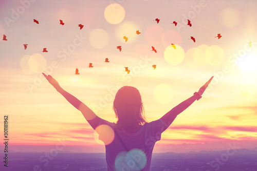 Freedom feel good and travel adventure concept. Copy space of silhouette woman rising hands on sunset sky at top of mountain and bird fly abstract background.