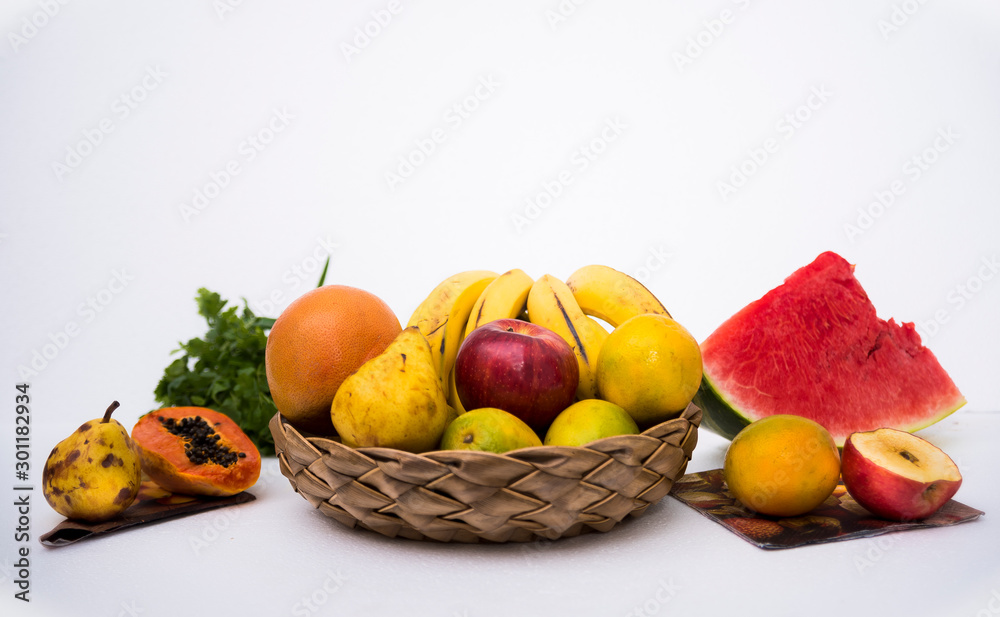 Several tropical fruits in a basket and spread all over a white table
