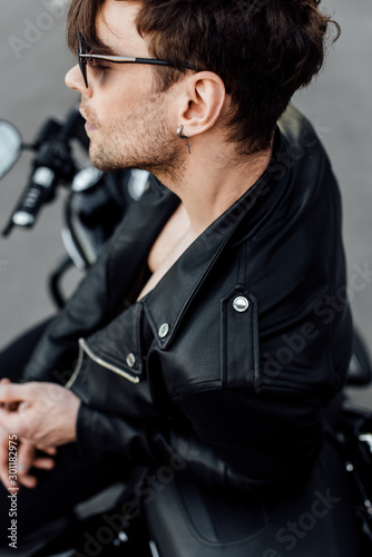 selective focus of young man in leather jacket sitting on motorcycle with closed eyes