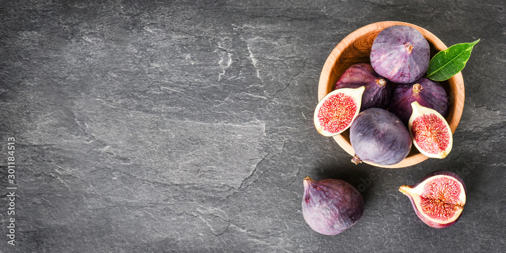 Fresh figs in round wooden bowl on dark stone table, space for text. Ripe fig fruits with leaves on black texture board. Banner or panorama concept top view. - obrazy, fototapety, plakaty 