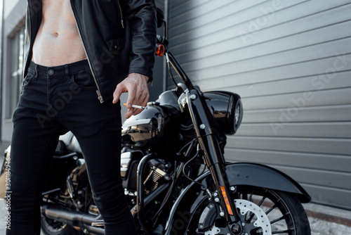 cropped view of man with naked torso holding cigarette and standing near motorcycle