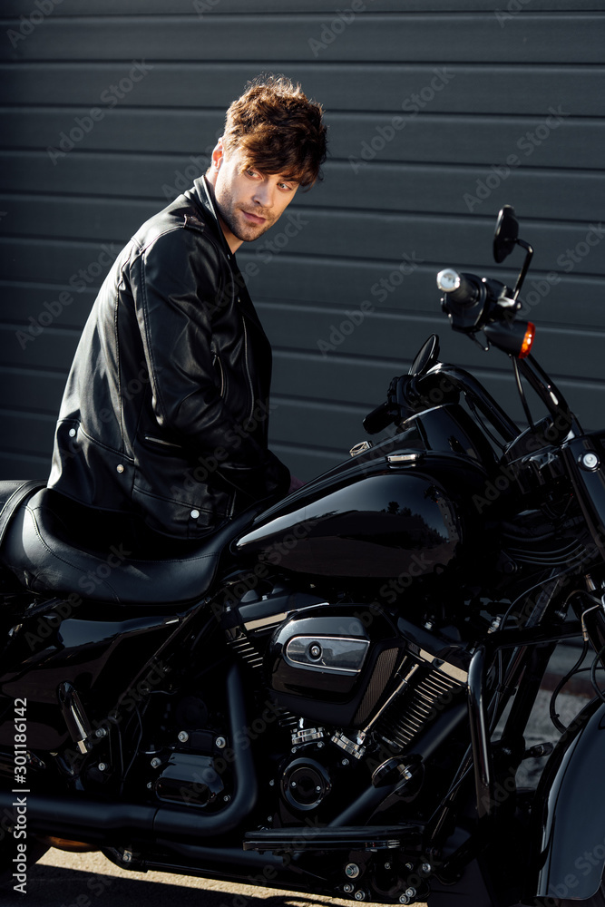 young motorcyclist in black leather jacket sitting on motorcycle