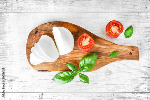 Tableau sur toile Fresh finest tomatoes on white rustic board with basil and mozzarella cheese top view