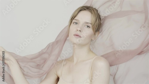 Girl on background of fluttering chiffon pink fabric. Gentle perfume. Nude makeup. The natural beauty of the girl. In studio. Slow motion fabric in wind.