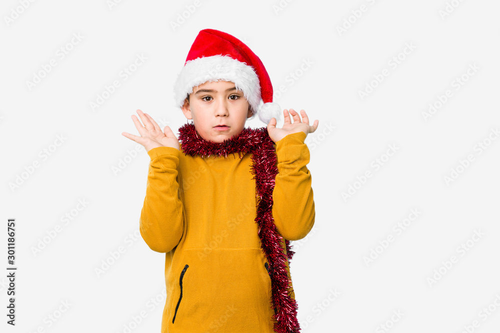 Little boy celebrating christmas day wearing a santa hat isolated surprised and shocked. Little boy celebrating christmas day wearing a santa hat isolated surprised and shocked.