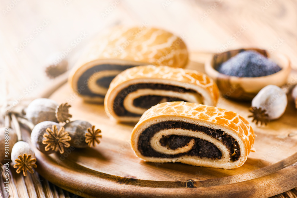 Poppy roll cake on wooden rustic table. Traditional christmas strudel with poppies heads and seed in background. Poppy roll cake on wooden rustic table. Traditional christmas strudel with poppies heads and seed in background.