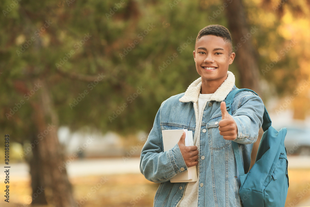 Portrait of teenage African-American student showing thumb-up outdoors - obrazy, fototapety, plakaty 