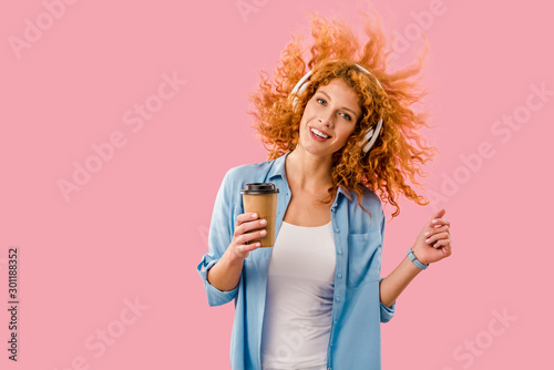 happy woman with coffee to go dancing and listening music in headphones, Isolated On pink