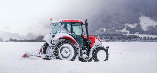Tractor in winter plowing street or road, agricultural and snow on fields.