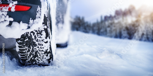 Winter tire detail in snowy mauntains. Car tires in snow with sun lights in background. © Milan