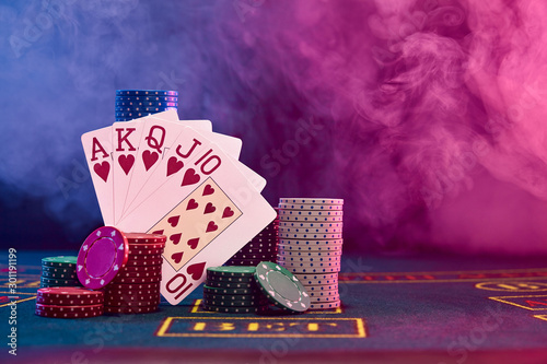 Winning combination in poker leaning on colored chips piles on blue cover of playing table. Black, smoke background, red and blue backlights. Casino. photo