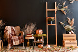 Beautiful autumn composition with wicker armchair near dark wall