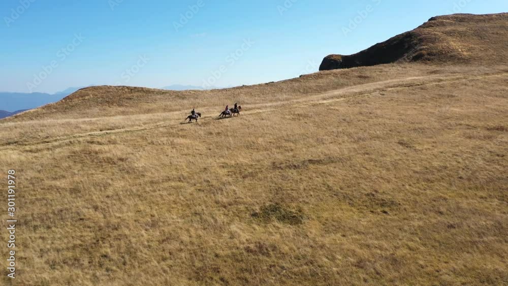 Aerial shot of people riding horses on a mountain in the fall. Three riders enjoy the perfect environment filled with warm colors. Aerial shot of people riding horses on a mountain in the fall. Three riders enjoy the perfect environment filled with warm colors.