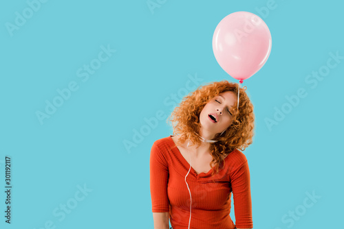 exhausted redhead woman with pink balloon isolated on blue