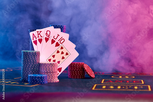 Winning combination in poker leaning on colored chips piles on blue cover of playing table. Black, smoke background, red and blue backlights. Casino.