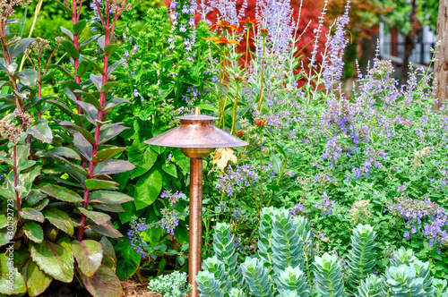 Slika na platnu Located beside a patio, a copper landscape lighting fixture adds structure and provides illumination and safety to this beautiful front garden