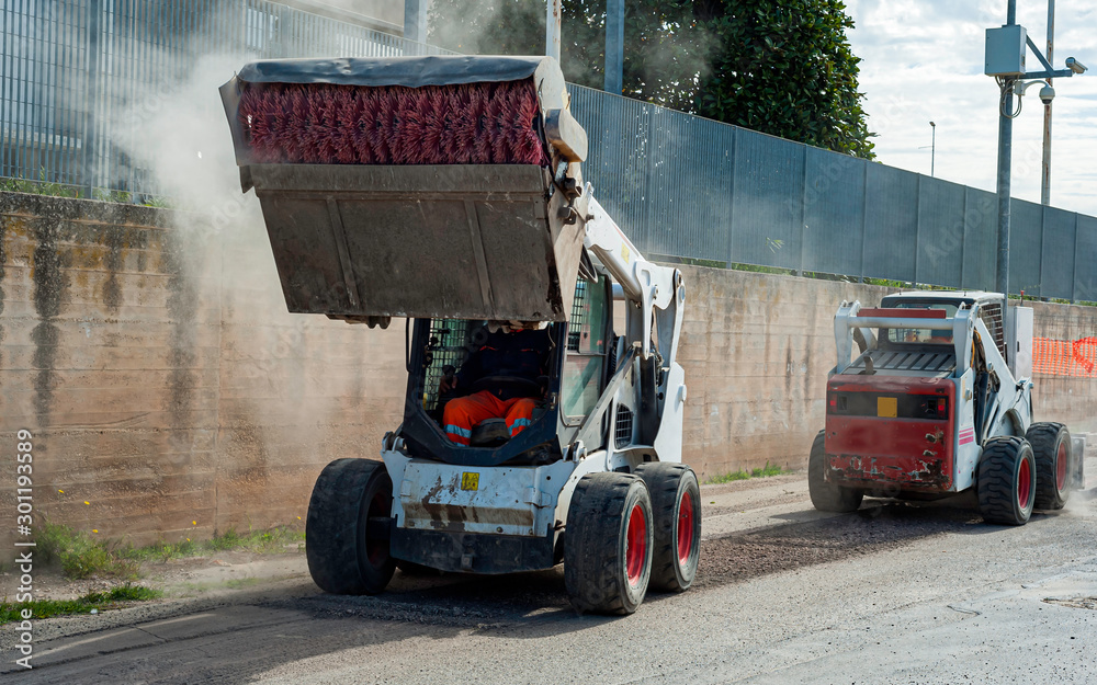 Fototapeta premium Milling drum for road milling machine and sweeper attachments mini excavator. Milling of asphalt for road reconstruction accessory for skid steer. Sweeper sweeps, collects and dumps dirt and debris.